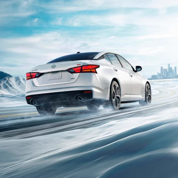 2027 Nissan Altima in white seen from behind driving in snowy landscape illustrating all-wheel drive at Hill Nissan in Winter Haven FL
