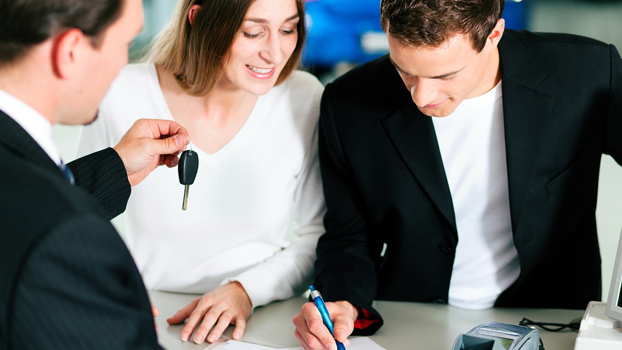 dealer offering car keys while person signing on papers